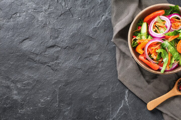 Fresh vegetable salad with lettuce tomato cucumber red onion and carrot in bowl on dark stone background healthy eating concept top view copy space