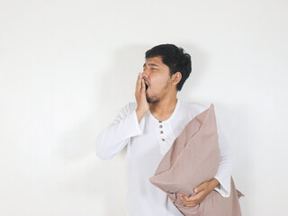 Handsome Asian man yawning while holding a pillow with a sleepy and tired expression