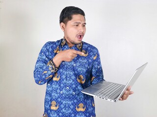 Indonesian civil servant man holding a laptop and pointing at the laptop he is holding with a...