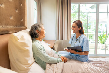 Asian woman doctor examine and consult senior patient on the bed in bedroom. Nurse or caregiver...