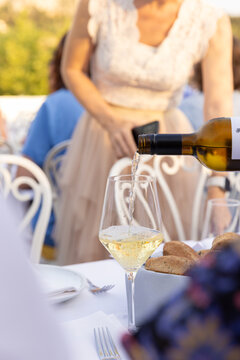 Waitstaff pouring glass of white wine into a customer's glass at an upscale lunch or brunch restaurant with a chic crowd. 