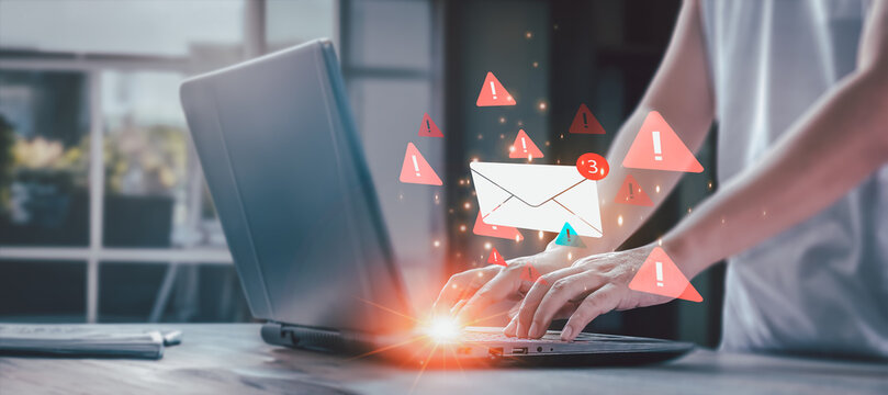 Cybersecurity alert concept. A person types on a laptop, bombarded by glowing red warning icons around an email notification, signifying a spam or phishing threat.