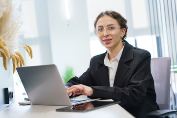 Fototapeta premium Professional woman engaged in work at a modern office desk showcasing a blend of concentration and determination in a bright space