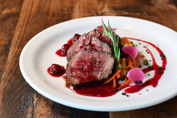 Sliced cooked veal served with julienne vegetables and cherry sauce, garnished with rosemary sprig