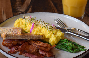 Breakfast plate with scrambled eggs, bacon, steamed asparagus and toasted bread