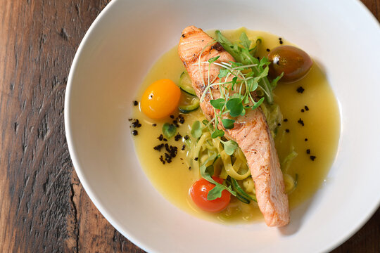 Grilled slamon fillet served over zucchini noodles in butter sauce on white plate