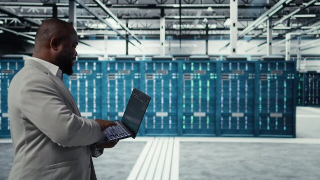 Data center developer writing code for resource optimization using notebook. Server room engineer deploying new builds to improve uptime using software on laptop, camera A