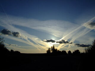 Dramatic sunset over a winding road, with vibrant clouds and crisscrossing contrails creating a...