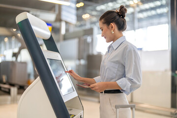 Confident woman traveler passenger with luggage using digital check in at airport kiosk, smart...