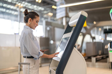 Confident woman traveler passenger with luggage using digital check in at airport kiosk, smart travel concept, modern airline automation, self service boarding, efficient travel technology experience