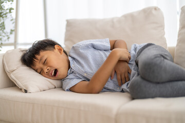 Portrait of sick unhappy little child asian boy touching belly stomach with suffering from stomach...