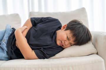 Portrait of sick unhappy little child asian boy touching belly stomach with suffering from stomach...