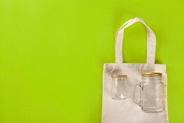 Eco bag with empty reusable empty bottles on light green background. top view