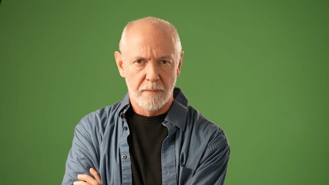 A mature man holds his face from tooth pain with one hand, showcasing a contemplative emotion. He stands against a solid green screen, highlighting his thoughtful demeanor.