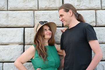 woman in green dress in hat and man in hat are near brick wall,