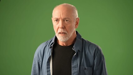 A mature man wearing glasses poses thoughtfully against a solid green screen background, evoking deep contemplation and emotion in his expression.