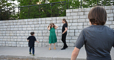 woman in green dress in hat and man in hat are near brick wall,
