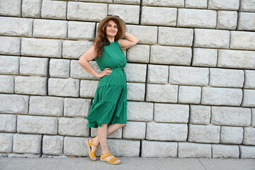 woman in green dress in hat is near brick wall,