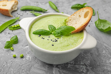 Tasty pea cream soup with basil and crouton served on grey table, closeup