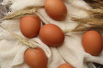 Raw eggs, fabric and spikes of wheat on wooden table, flat lay
