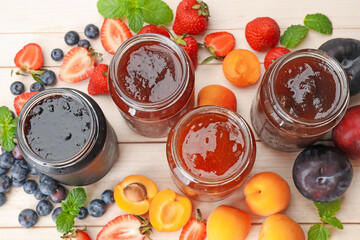 Tasty sweet jams in jars surrounded by ingredients on light wooden table, flat lay