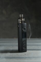 One electronic smoking device in smoke on wooden table against grey background, closeup