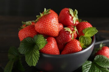Fresh ripe strawberries and leaves in bowl on black table, closeup