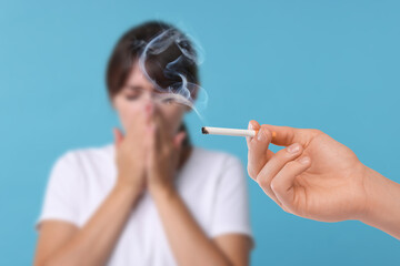 Passive smoking. Woman covering her nose with hands because of man smoking nearby on light blue...