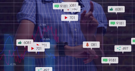 Gesturing female wearing blue-white striped shirt exploring floating icons and graphs at brick wall