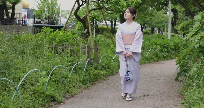 緑の木々の中を歩く和服を着た若い日本人女性