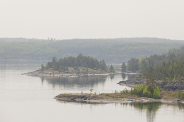 Peaceful, mist-covered forested islands surrounded by calm lake water, creating a serene and moody...