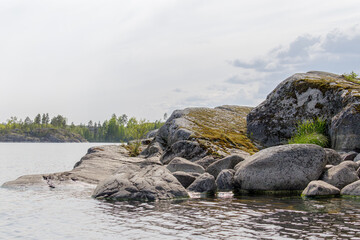 A peaceful lakeside scene showing large moss-covered rocks and boulders along the shore, with calm...