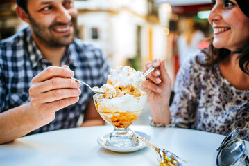Happy couple eating ice cream dessert outdoors at a cafe