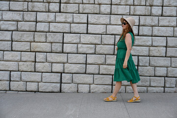 woman in green dress in hat is near brick wall,