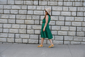 woman in green dress in hat is near brick wall,