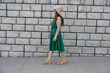 woman in green dress in hat is near brick wall,