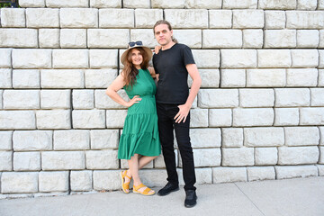 woman in green dress in hat and man in hat are near brick wall,