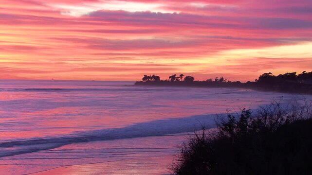 Purple and orange waves reflect the sunset and splash a Santa Barbara, California beach near the UCSB campus.