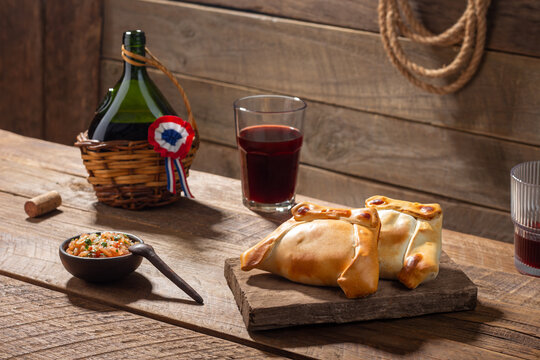 Two empanadas, a typical Chilean dish for September 18th, along with a bottle and glasses of red wine in a rustic setting.