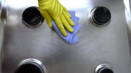 Female hand in yellow gloves wipes the kitchen stove with dry sponge. Сlose up of kitchen stove in the process of cleaning. House cleaning service