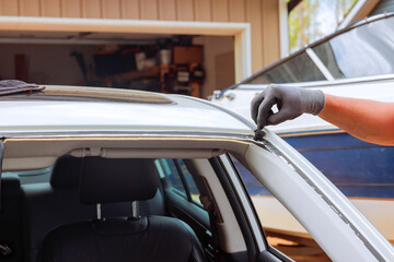 Worker works on sealing window trim of car in garage filled with car maintenance tools.