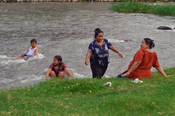 While one mother walks toward the riverbank, another sits and watches. The children play joyfully...