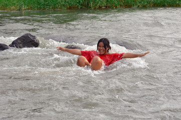 Floating joyfully on her back, a teenage girl opens her arms wide and smiles, enjoying the cool water and gentle stream under overcast light.
