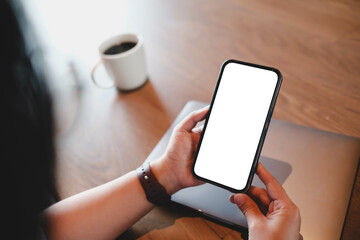 Over the shoulder view of a person holding a smartphone with a blank white screen. Mockup scene...