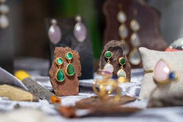 Close-up of elegant green gemstone earrings set on natural stone, surrounded by various jewelry pieces, capturing a blend of elegance and nature in a jewelry showcase.