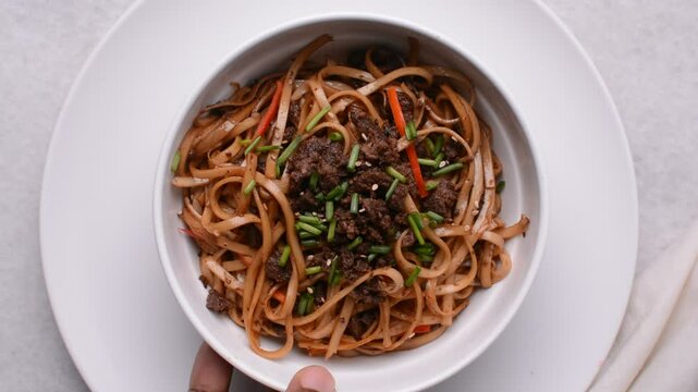 Overhead view of mongolian ground beef noodles in a white bowl, top view of ground beef noodles with green and red pepper	