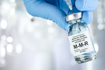 Healthcare concept with a hand in blue medical gloves holding MMR, measles, mumps, and rubella, vaccine vial