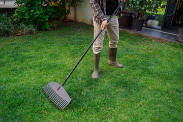 Unrecognizable man gardener on beautiful cut grass using garden rake 