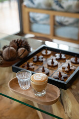 Hand holding a glass of latte on a wooden table with a blurred background.