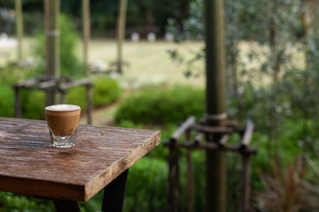 Hand holding a glass of latte on a wooden table with a blurred background.